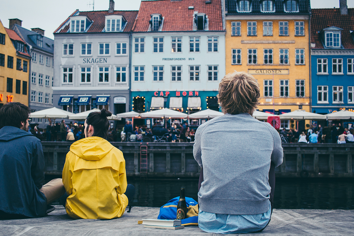 Personer sitter ved bryggekanten i sentrum. Foto.