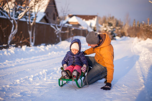 Foto, Far med datter på kjelke i en stille, snødekket gate.