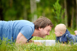 Foto: Far og baby ligger og ser på hverandre i gresset