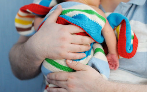 Foto: Mann holder en baby, intullet i et stripete teppe