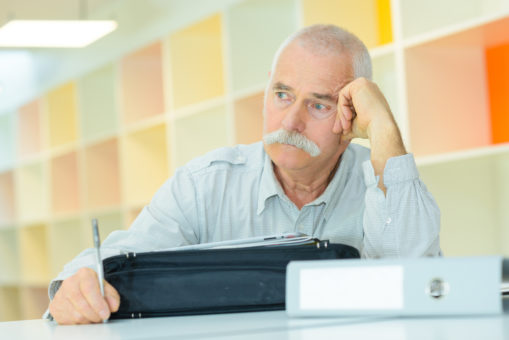 Foto: Eldre mann sitter ved pulten\, lener hodet i hånden og ser betenkt ut