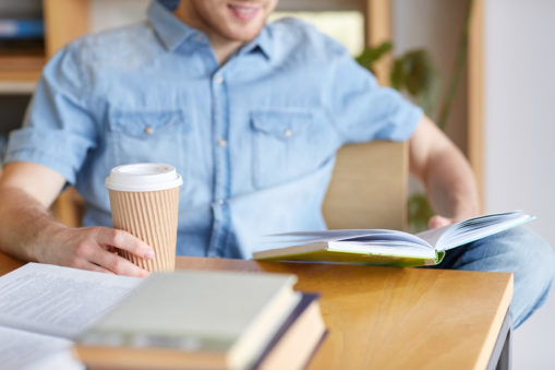 Foto: Mann leser med kaffekopp i den ene hånden og bok i den andre