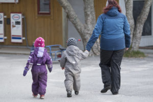 Foto av voksen som går sammen med to små barn og leier det ene barnet