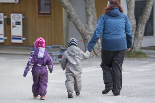 Foto av voksen som går sammen med to små barn og leier det ene barnet