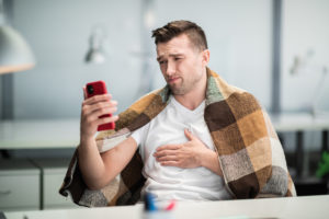 Syk mann med pledd over skuldrene sender SMS