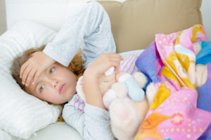 Foto: Sykt barn i sengen med kosedyr og et fargerikt teppe