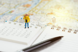 Kalender plassert på et kart for planlegging av ferie, Med en liten figur av en pack-packer stående midt i kalenderen.