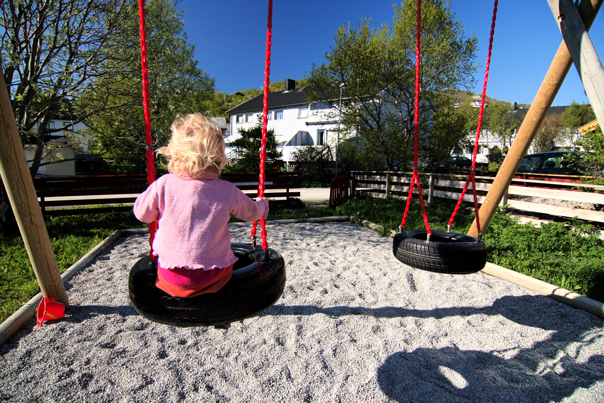 Foto: Lite barn, kledd i rosa sitter med ryggen til på en husk, alne