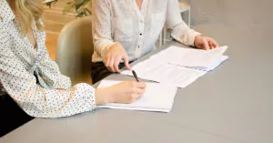 To kvinner jobber med papirer på en pult. Foto.