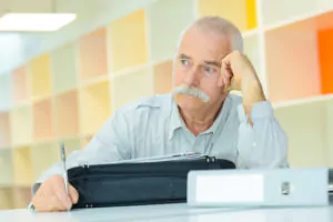 Foto: Eldre mann sitter ved pulten\, lener hodet i hånden og ser betenkt ut