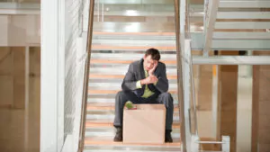 Foto; Man sitter nedbrutt i en trapp med en flyttekasse foran seg