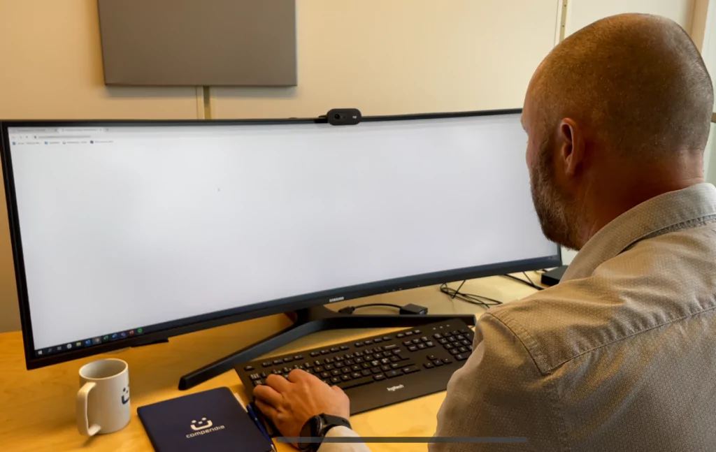 Foto: Mannsitter på kontor med stor PC-skjerm