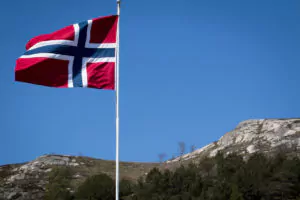 Foto: Norsk flagg mot blå himmel og fjell i bakgrunnen